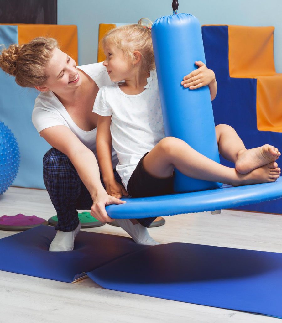 A physical therapist helping a child balance on a swing